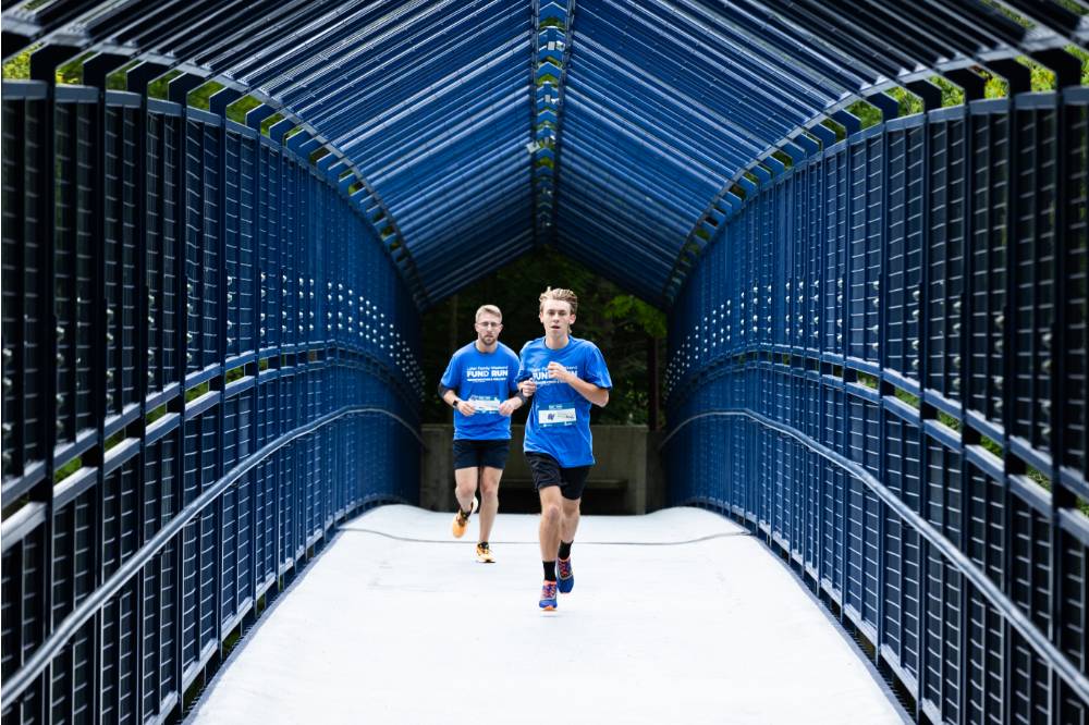 Individuals in blue shirts running through little mac bridge